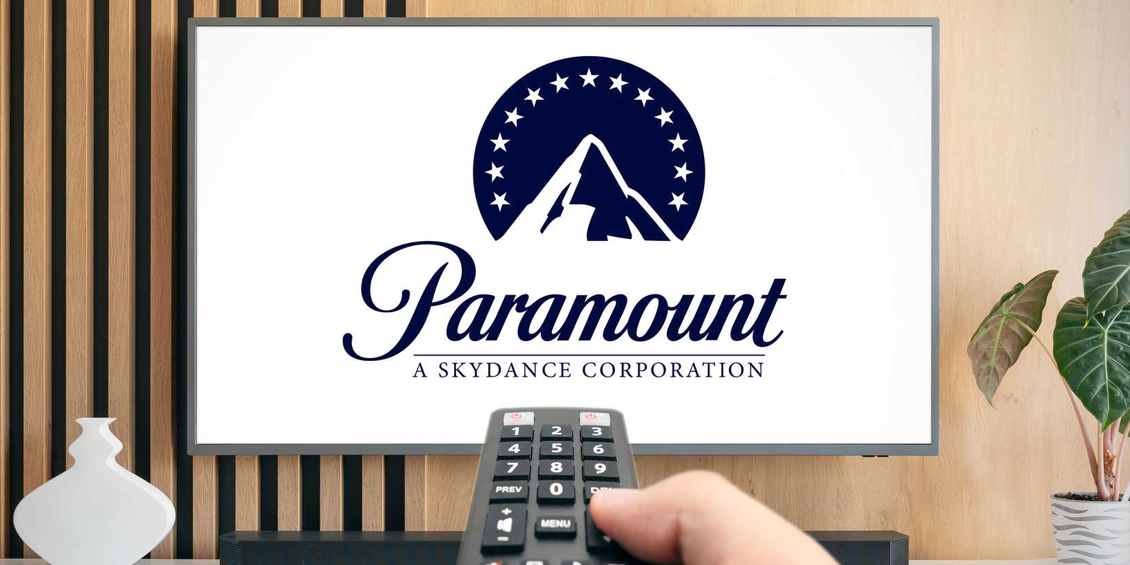 A hand holding a remote pointing at the Paramount logo