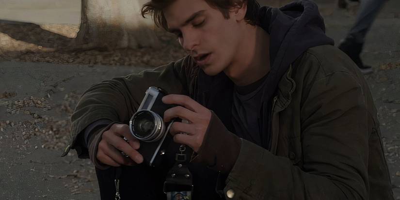 Peter Parker sitting on the ground looking at his camera in The Amazing Spider-Man