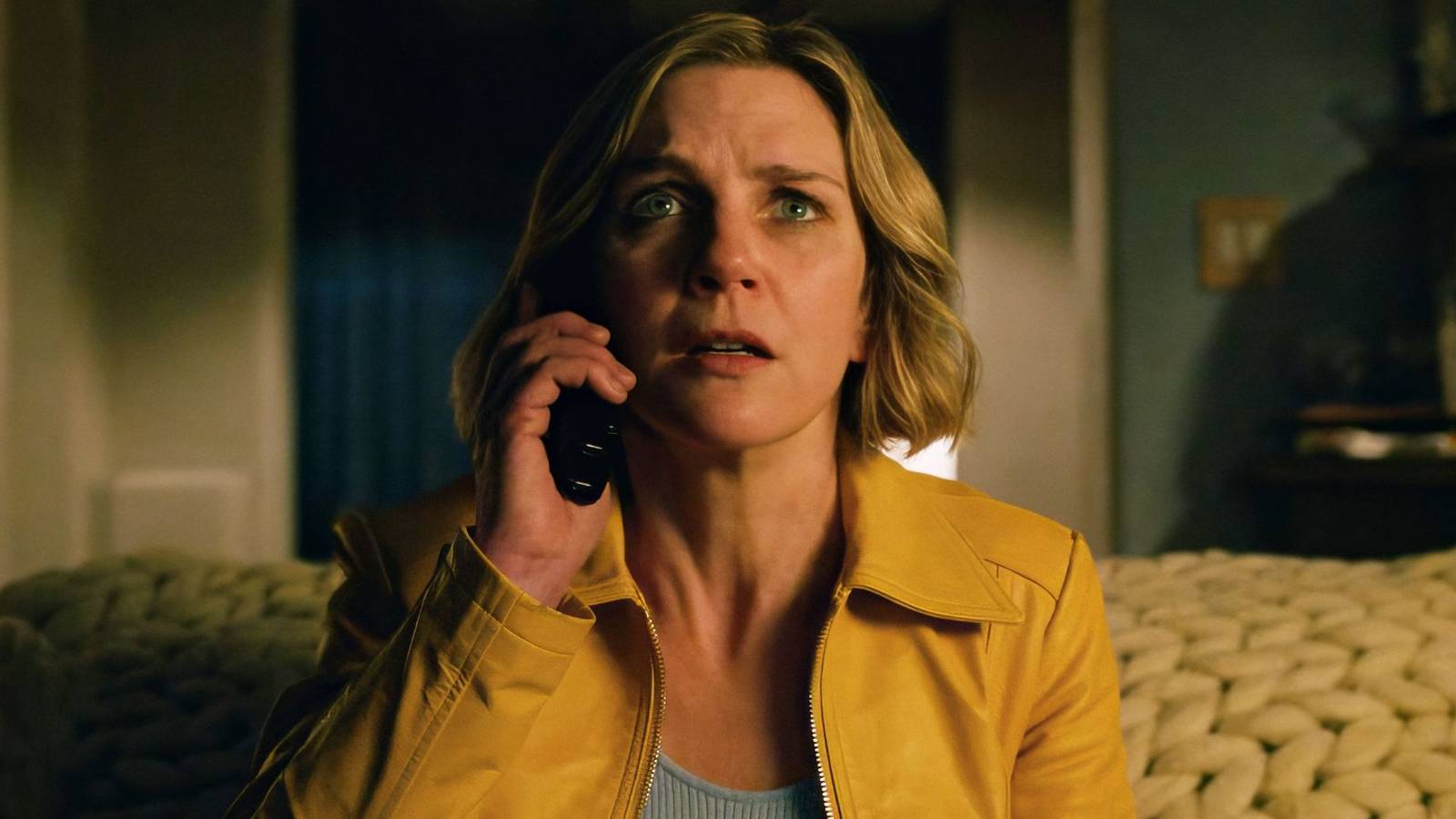 Rhea Seehorn in a yellow leather jacket on the phone while sitting on her bed in Pluribus Episode 1.