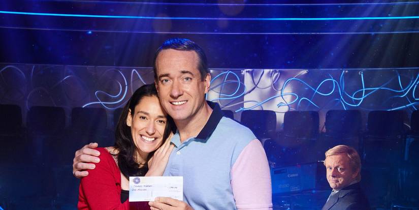 Sian Clifford and Matthew Macfadyen hug on a game show with Michael Sheen in the background in Quiz.