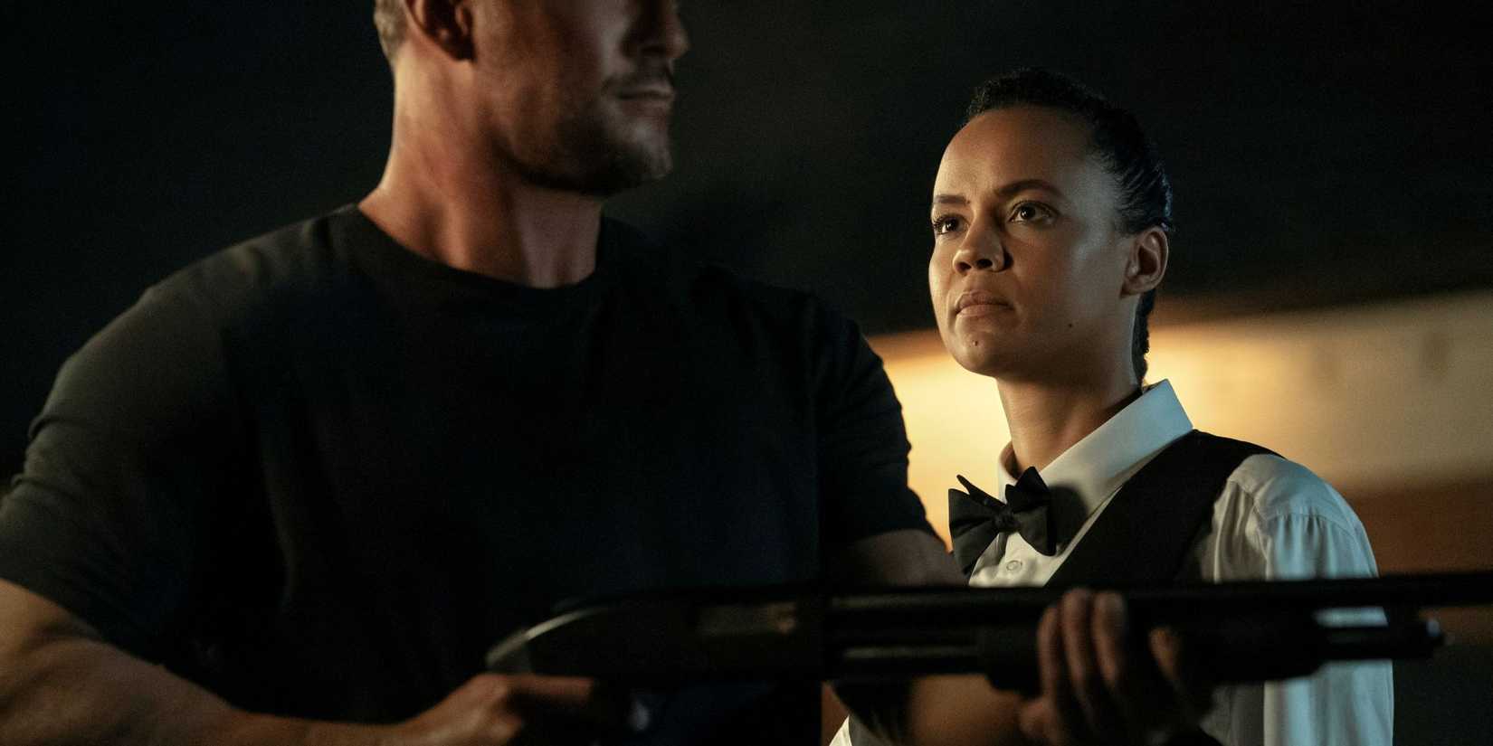 Maria Sten as Neagley dressed as a waiter behind Alan Ritchson as Jack Reacher holding a gun in Reacher.