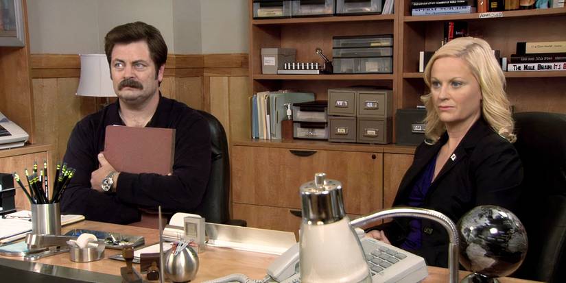 Ron and Leslie sit at a desk, looking concerned, in Parks and Recreation.