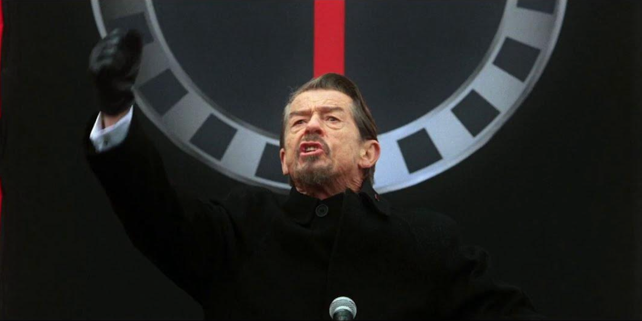 Adam Sutler (John hurt) talking heatedly at a podium in 'V for Vendetta'
