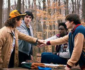 The OG Stranger Things party: Dustin, Mike, Lucas, and Will put their hands together while outside.