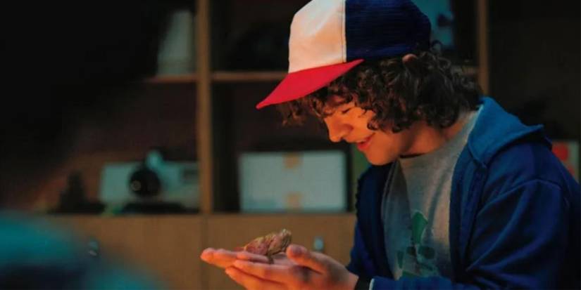 Gaten Matarazzo as Dustin holding a small creature named Dart and smiling in Stranger Things.