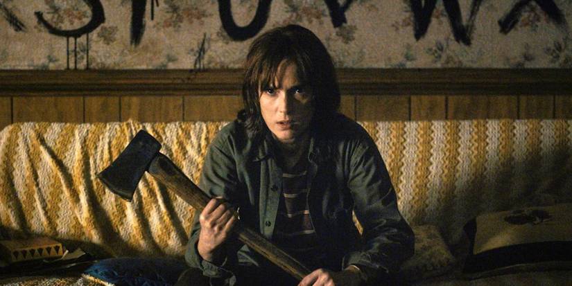 Joyce Byers (Winona Ryder) sitting on her couch with an ax in 'Stranger Things' Season 1.
