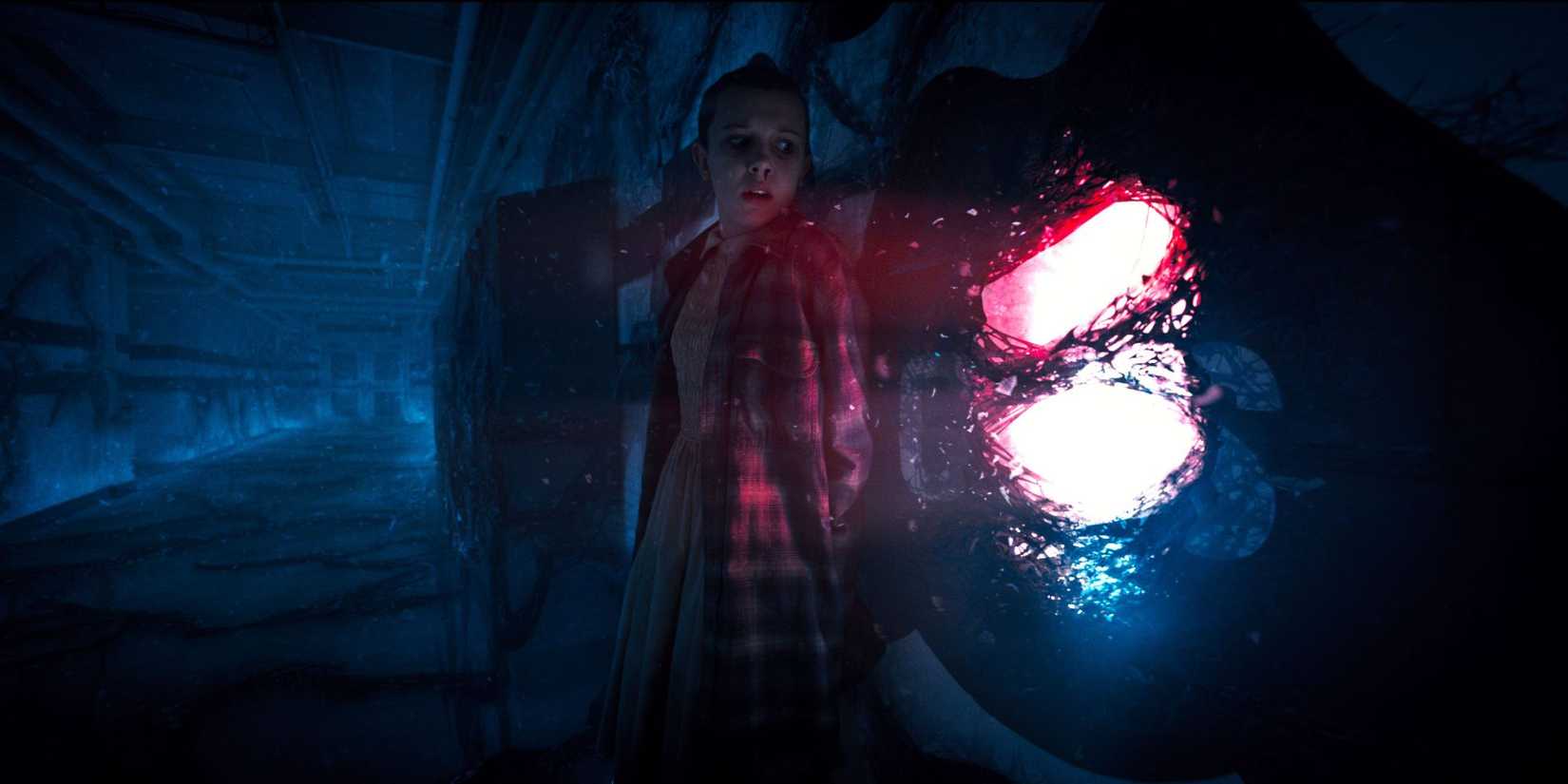 Millie Bobby Brown as Eleven stands with her back against a portal in Stranger Things.