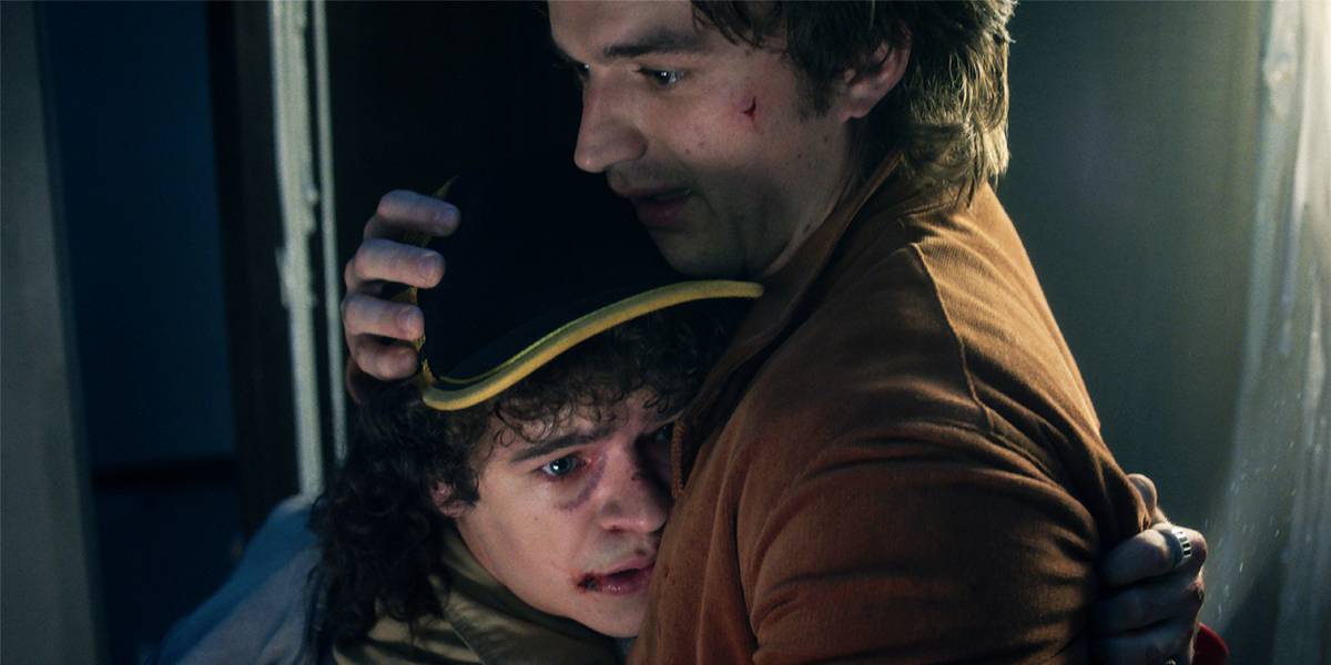 Steve Harrington abraçando Dustin Henderson, ambos com expressões assustadas.