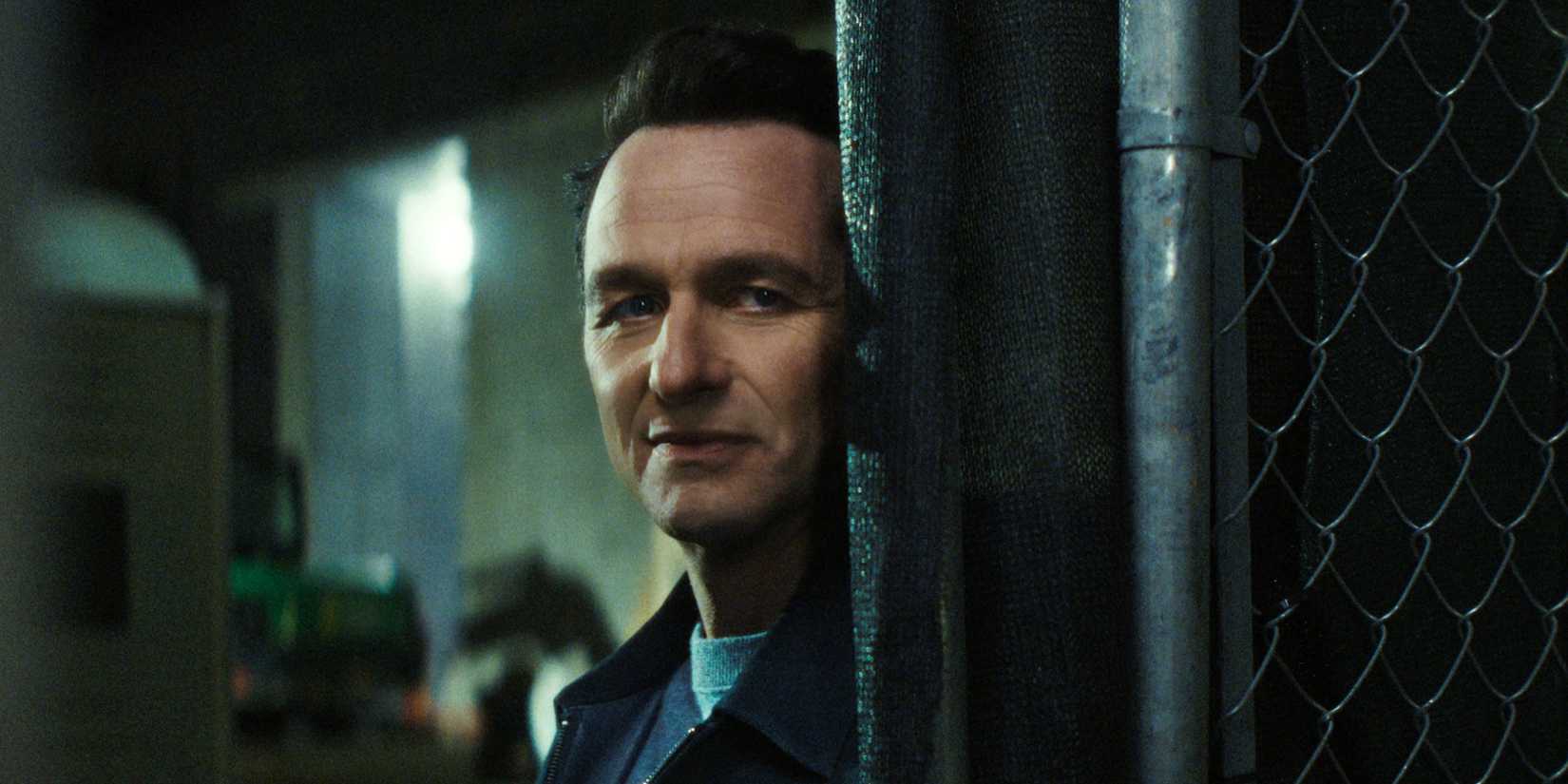 Matthew Rhys as Nile Jarvis leaning on a fence and looking like he's up to something in The Beast in Me