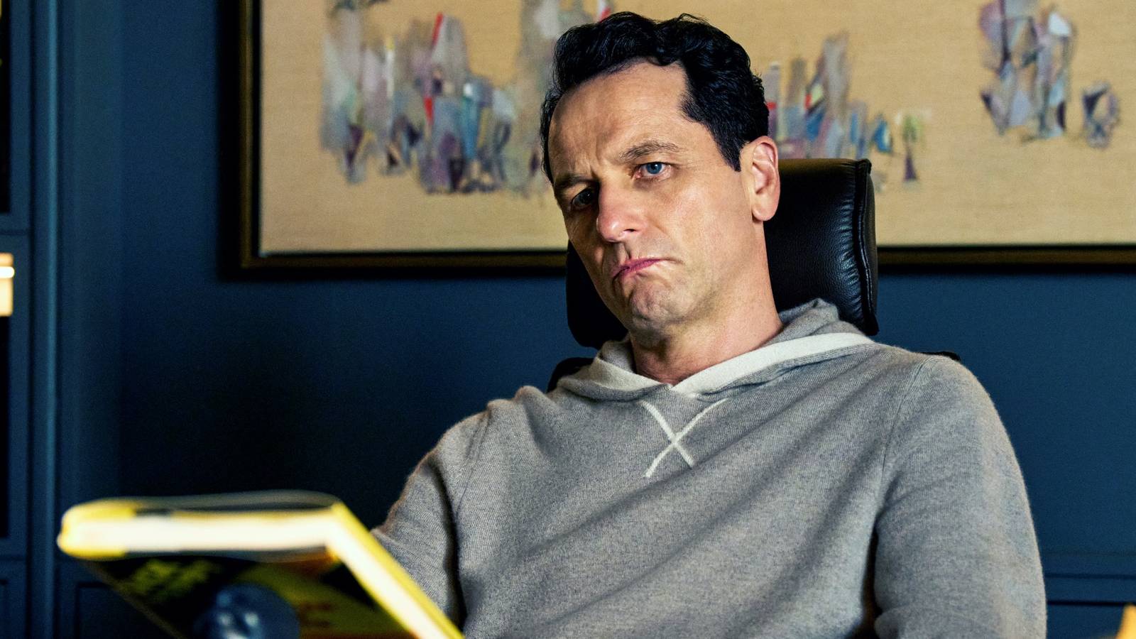 Matthew Rhys as Nile Jarvis sitting at a desk while holding a book in front of him in The Beast in Me