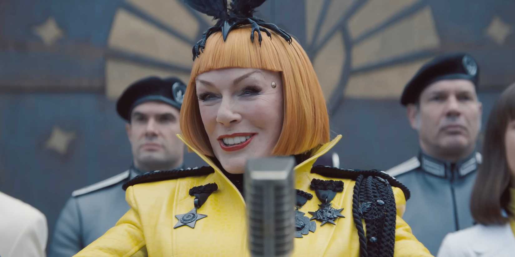 Glenn Close as Drusilla Sickle speaking to a microphone in The Hunger Games: Sunrise on the Reaping