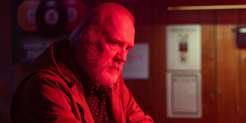 Tracy Letts as Frank Martin sitting at a bar while bathed in red light in The Lowdown