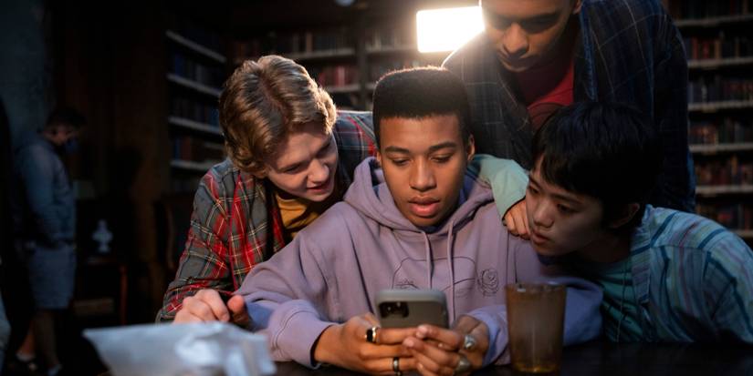 Igby Rigney as Kevin, Chris Sumpter as Spencer, Sauriyan Sapkota as Amesh, and Aya Furukawa as Natsuki look at a phone on 'The Midnight Club.'