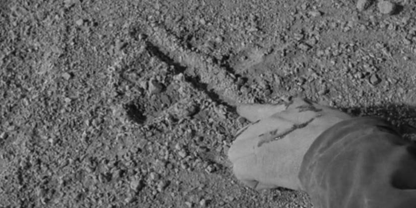 A closeup of a hand drawing something in dry soil in The Twilight Zone's I Shot an Arrow into the Air.