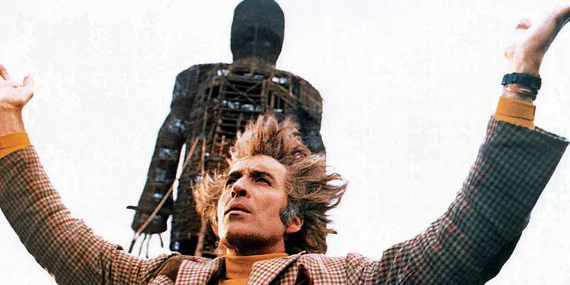 Lord Summerisle stands in front of a large wooden man in The Wicker Man.