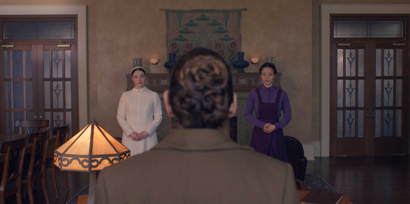 Lucy Halliday and Chase Infiniti stand listening to a woman with her back to camera in The Testaments.