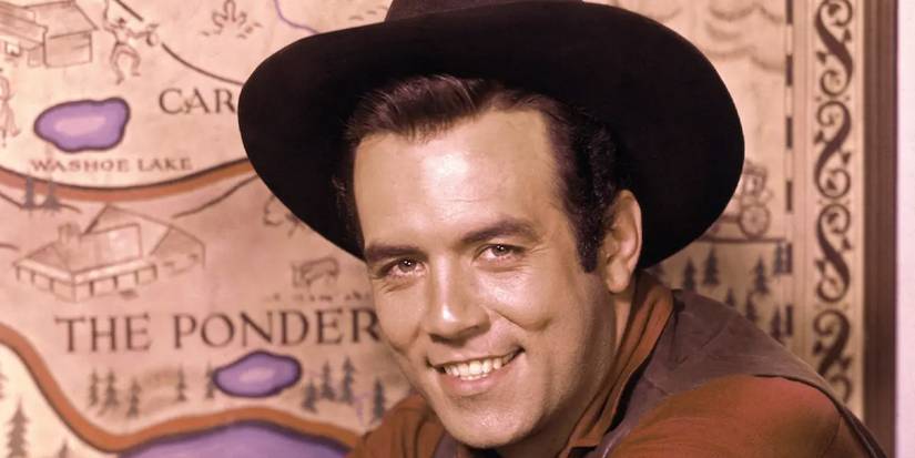 Pernell Roberts smiles as Adam Cartwright in front of a map of the Ponderosa on 'Bonanza'