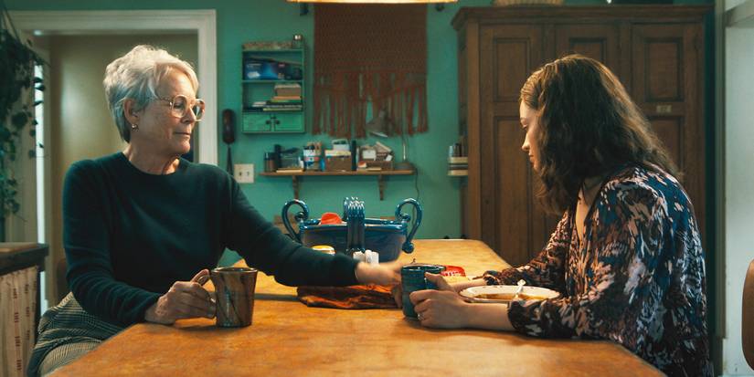 Helen reaches across a kitchen island to touch Ella's hand as they sit together with tea.