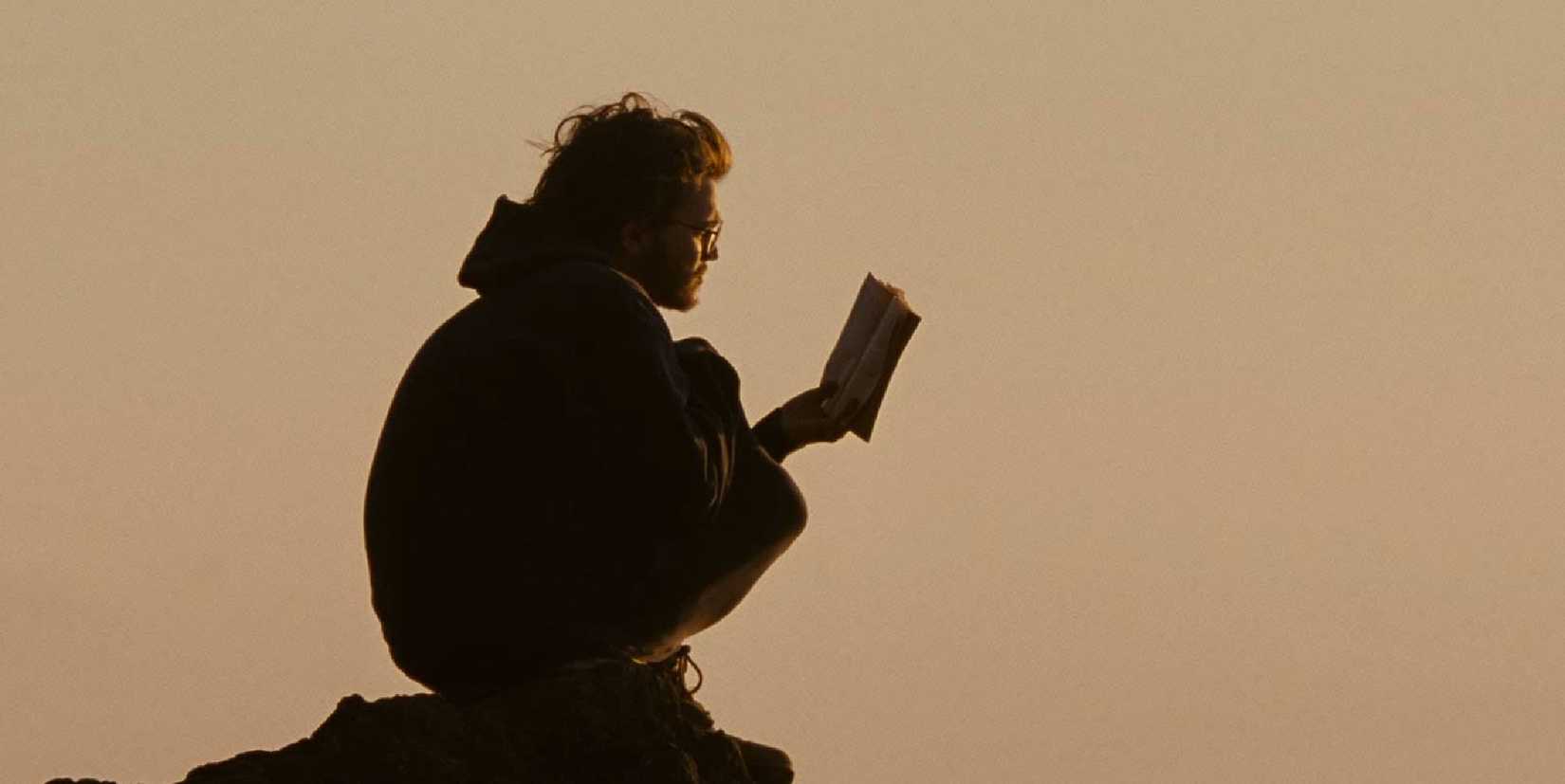 Emile Hirsch as Christopher reading in Into the Wild while sitting on the top of a mountain