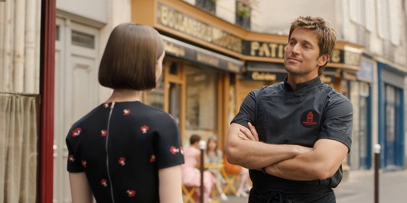 Gabriel with his arms folded talking to Emily in Emily in Paris.
