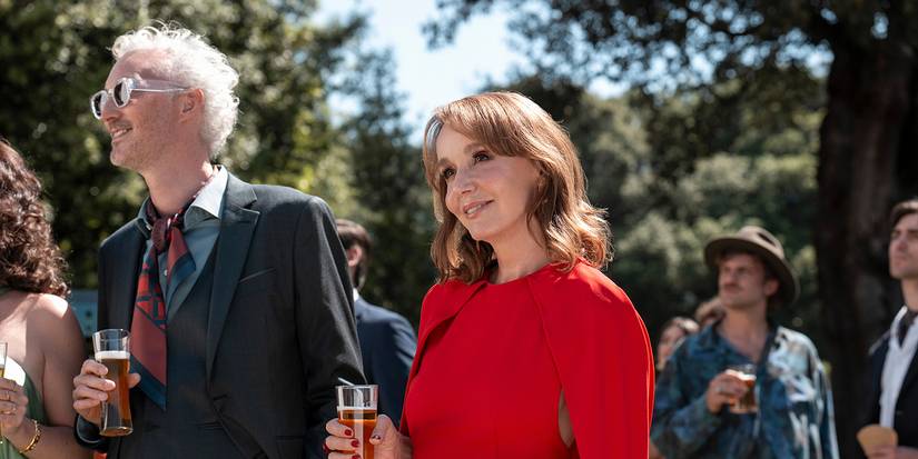 Sylvie smiling in a red dress with Luc in Emily in Paris.