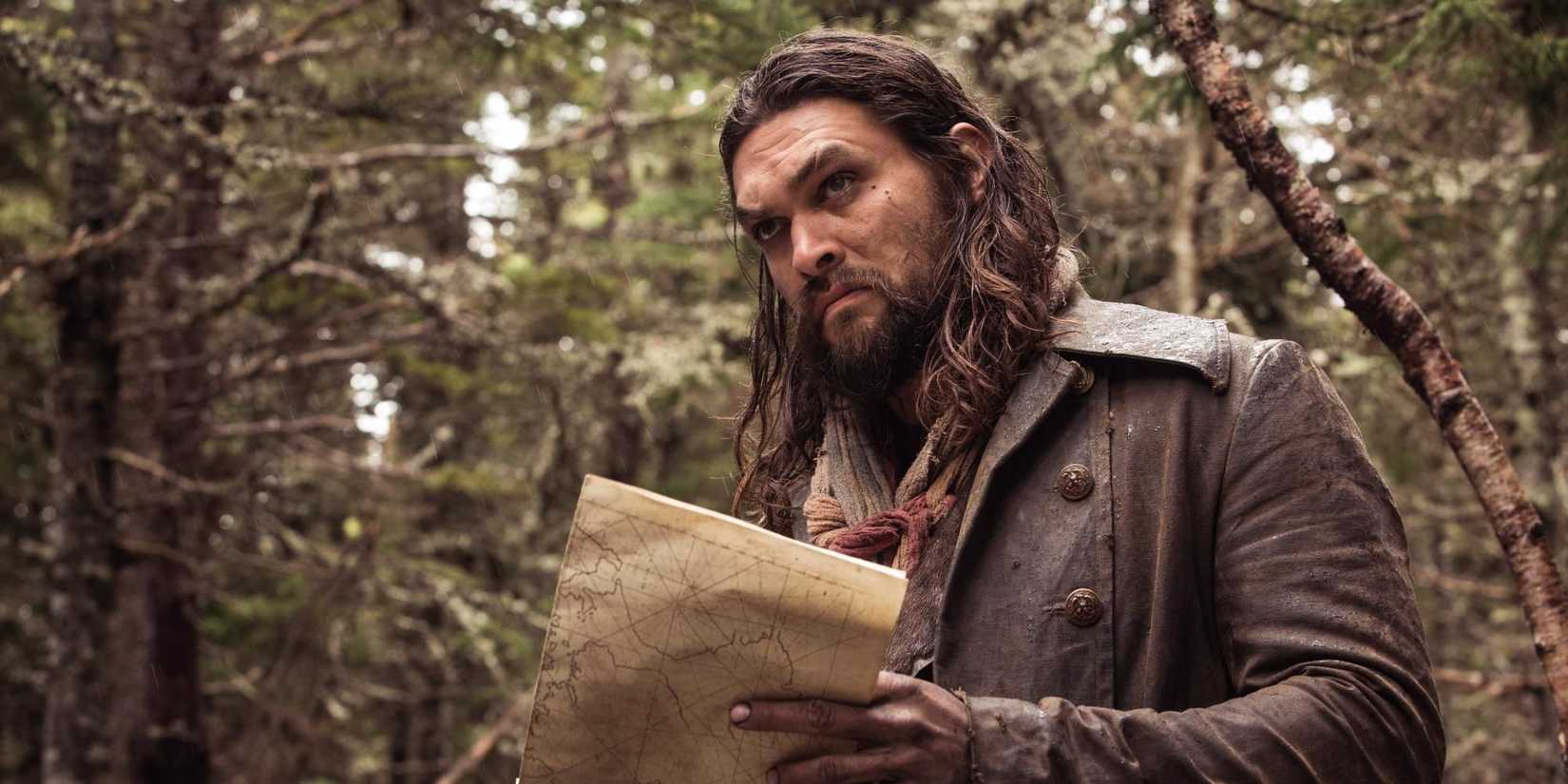 Jason Momoa with long hair stands in the woods and holds a map, looking to the distance in Frontier.