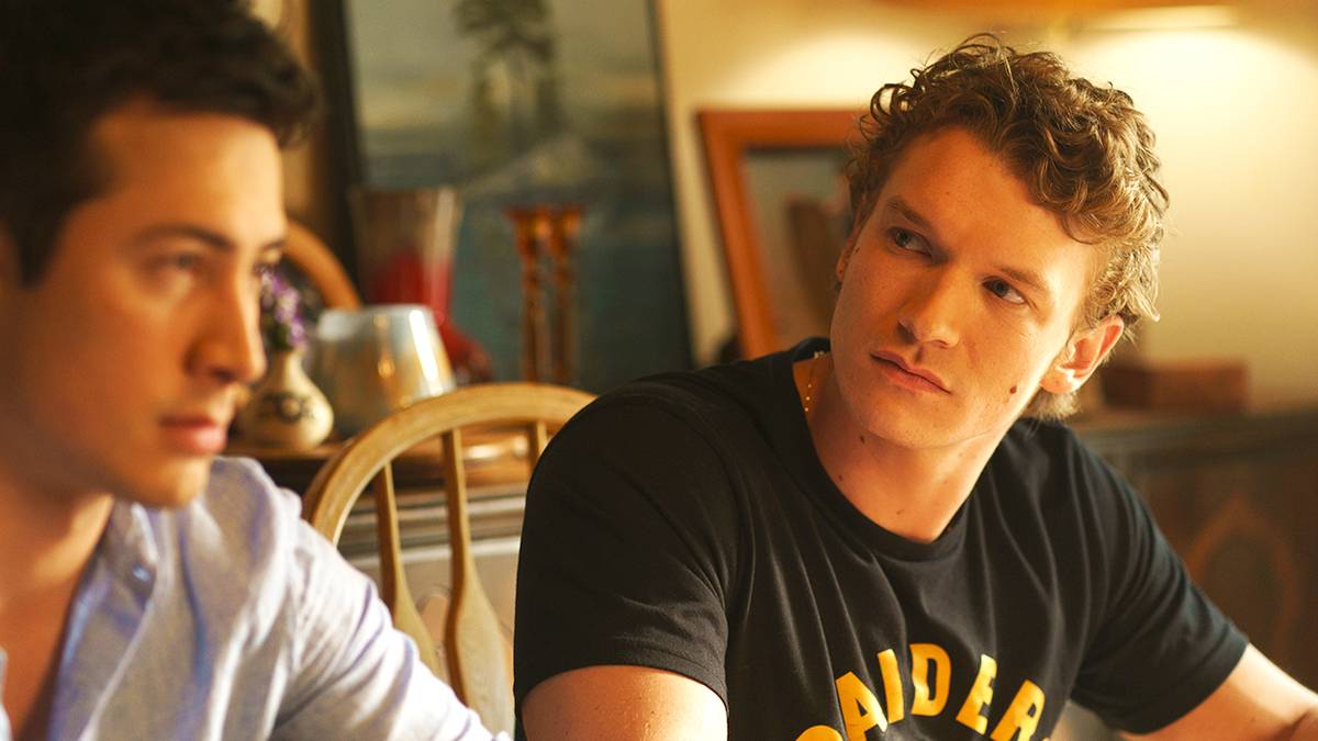 Connor Storrie and Hudson Williams looking tense sitting at a table in the Heated Rivalry finale.