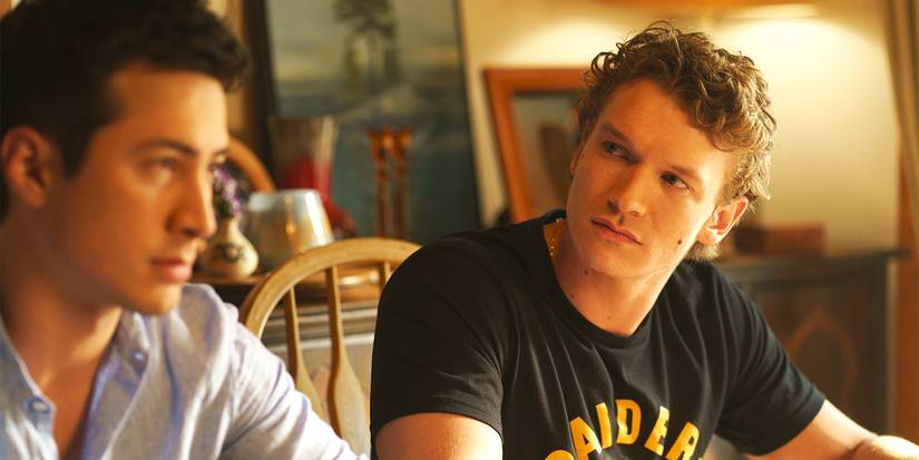 Connor Storrie and Hudson Williams looking tense sitting at a table in the Heated Rivalry finale.