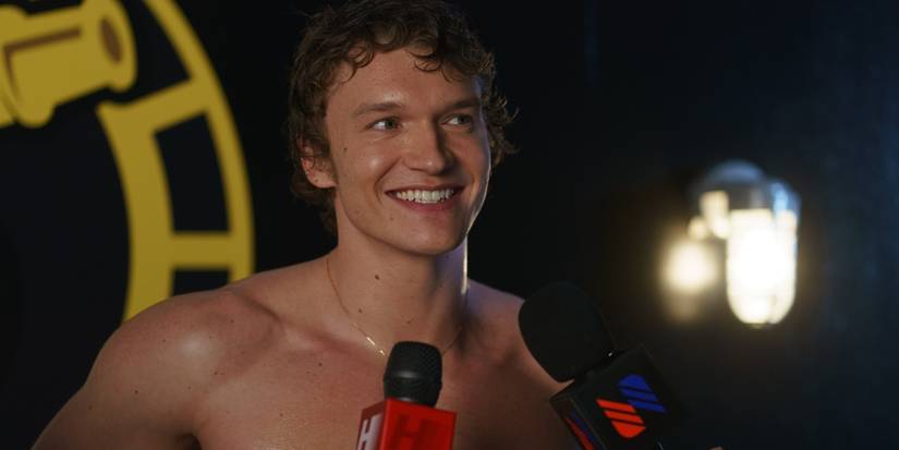 Connor Storrie as Ilya Rozanov smiling and talking to reporters without a shirt on in 'Heated Rivalry.'