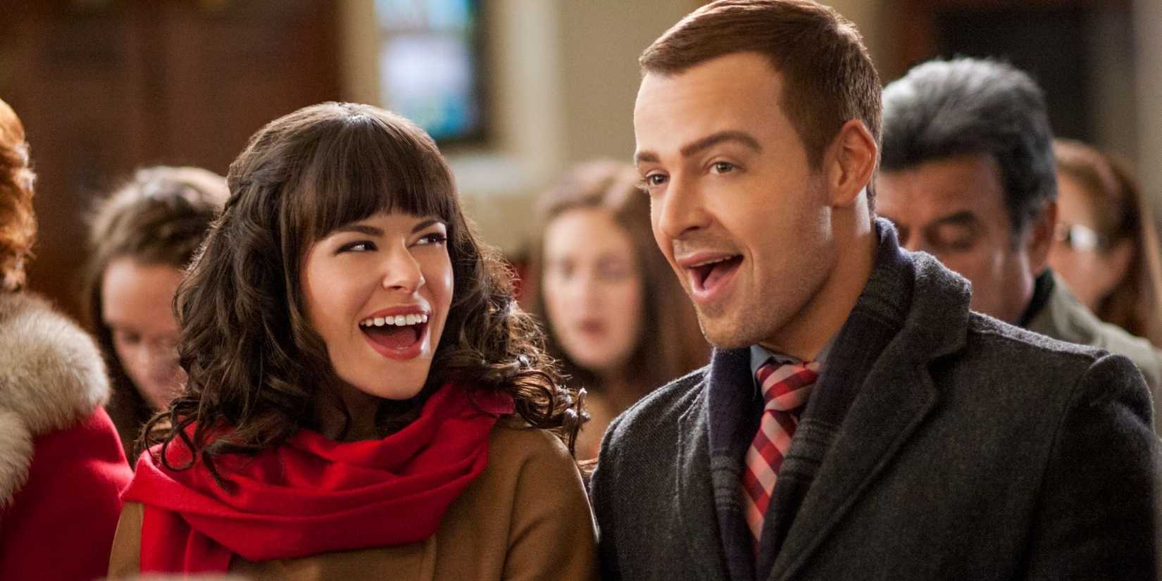 Emily Hampshire and Joey Lawrence sing with others in a still from Hitched for the Holidays.