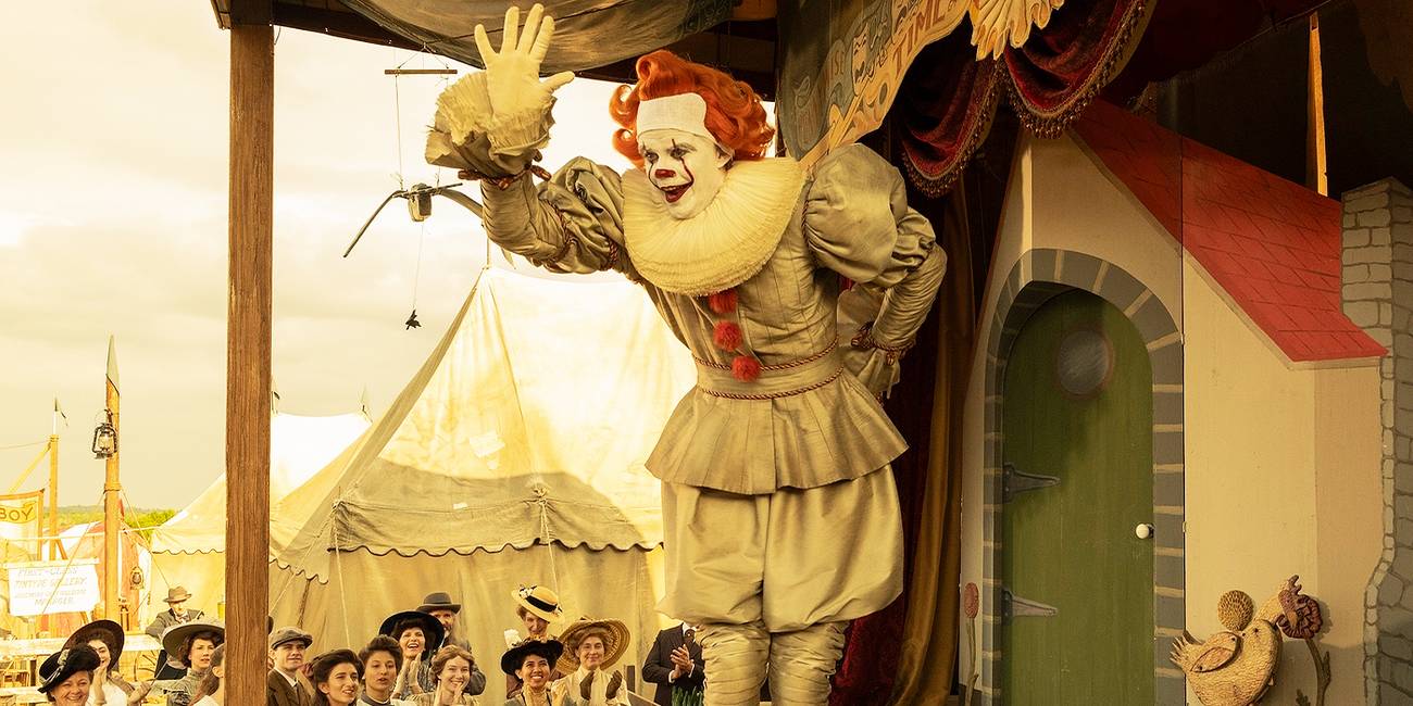 Bill Skarsgård's Pennwise smiling and waving to a crowd in IT: Welcome to Derry.