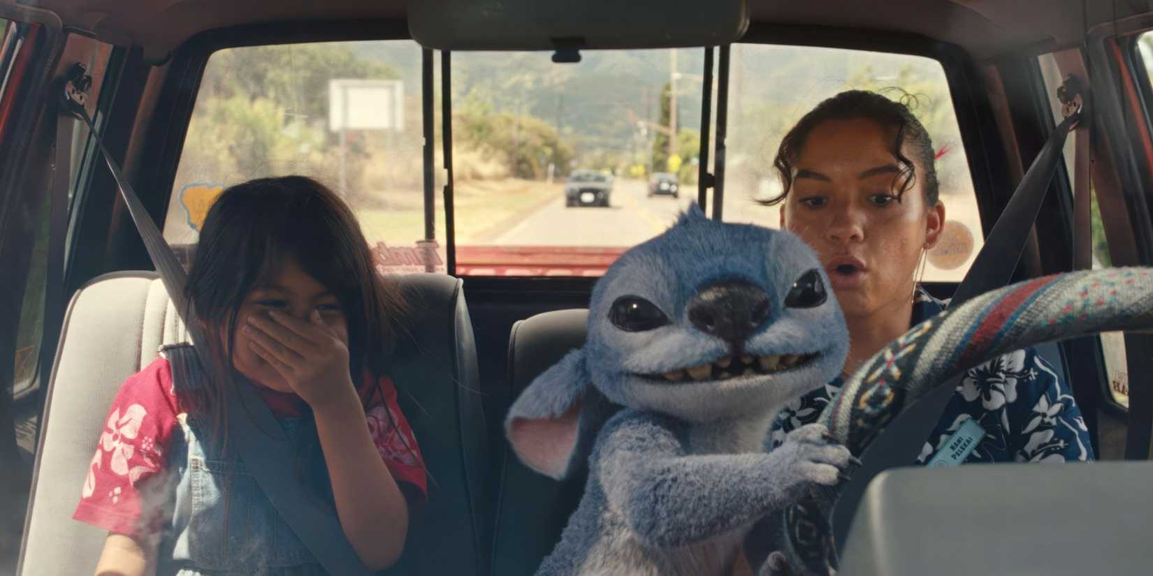 Stitch (Chris Sanders) takes the wheel of a car with Maia Kealoha and Sydney Agudong inside in Lilo & Stitch.