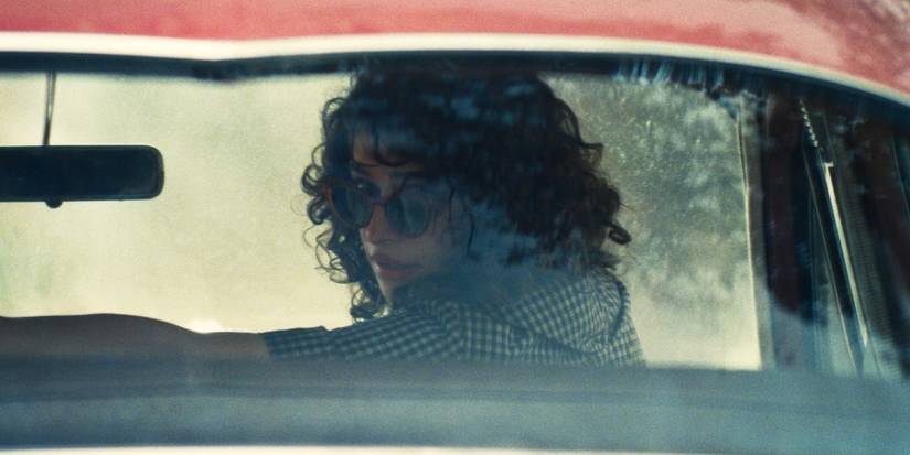 Odessa A'zion looks behind her from the passenger seat of a car in Marty Supreme