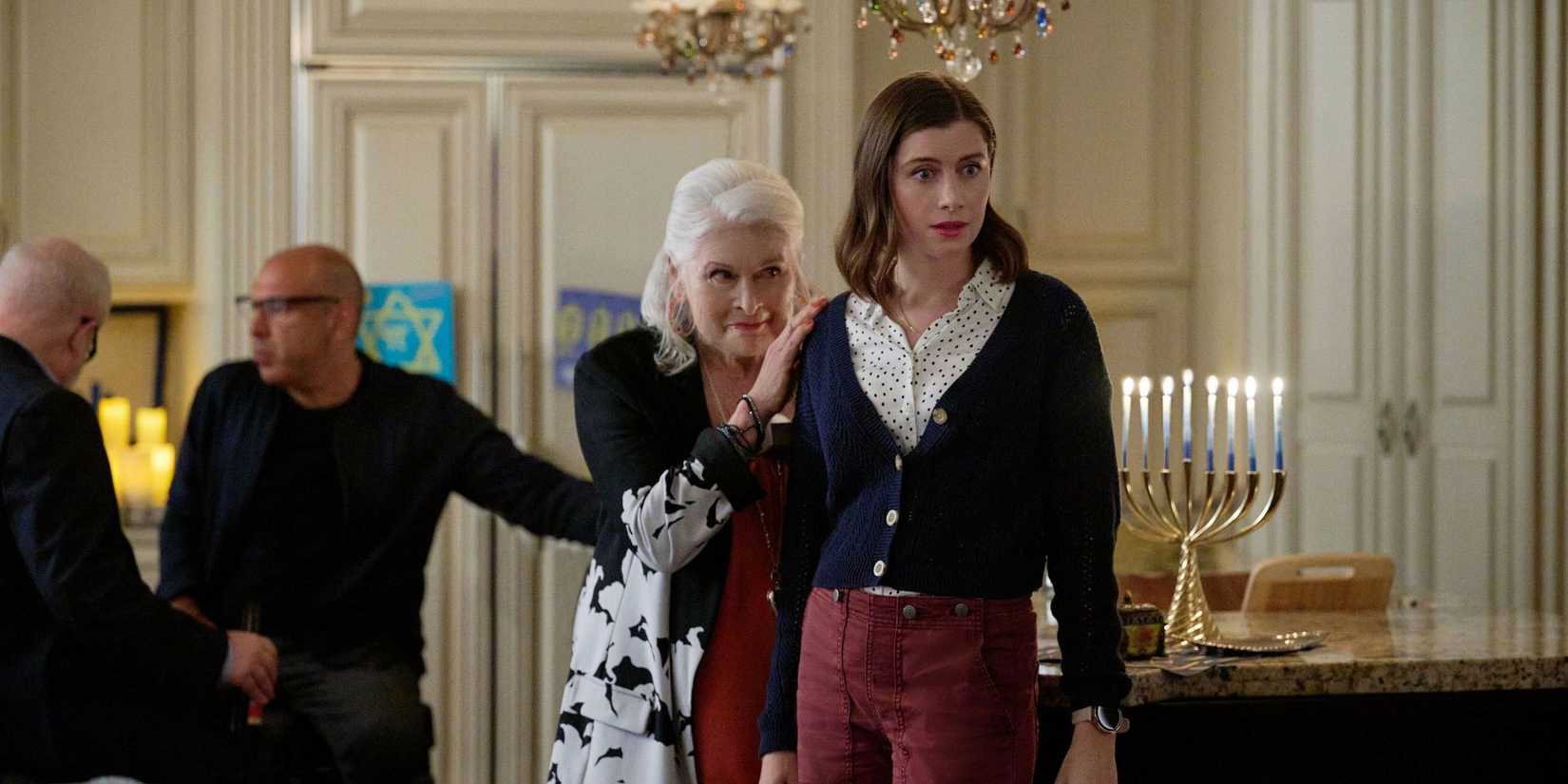 Vic Michaelis as Rachel looks surprised with an older woman behind her at a party in Round and Round.