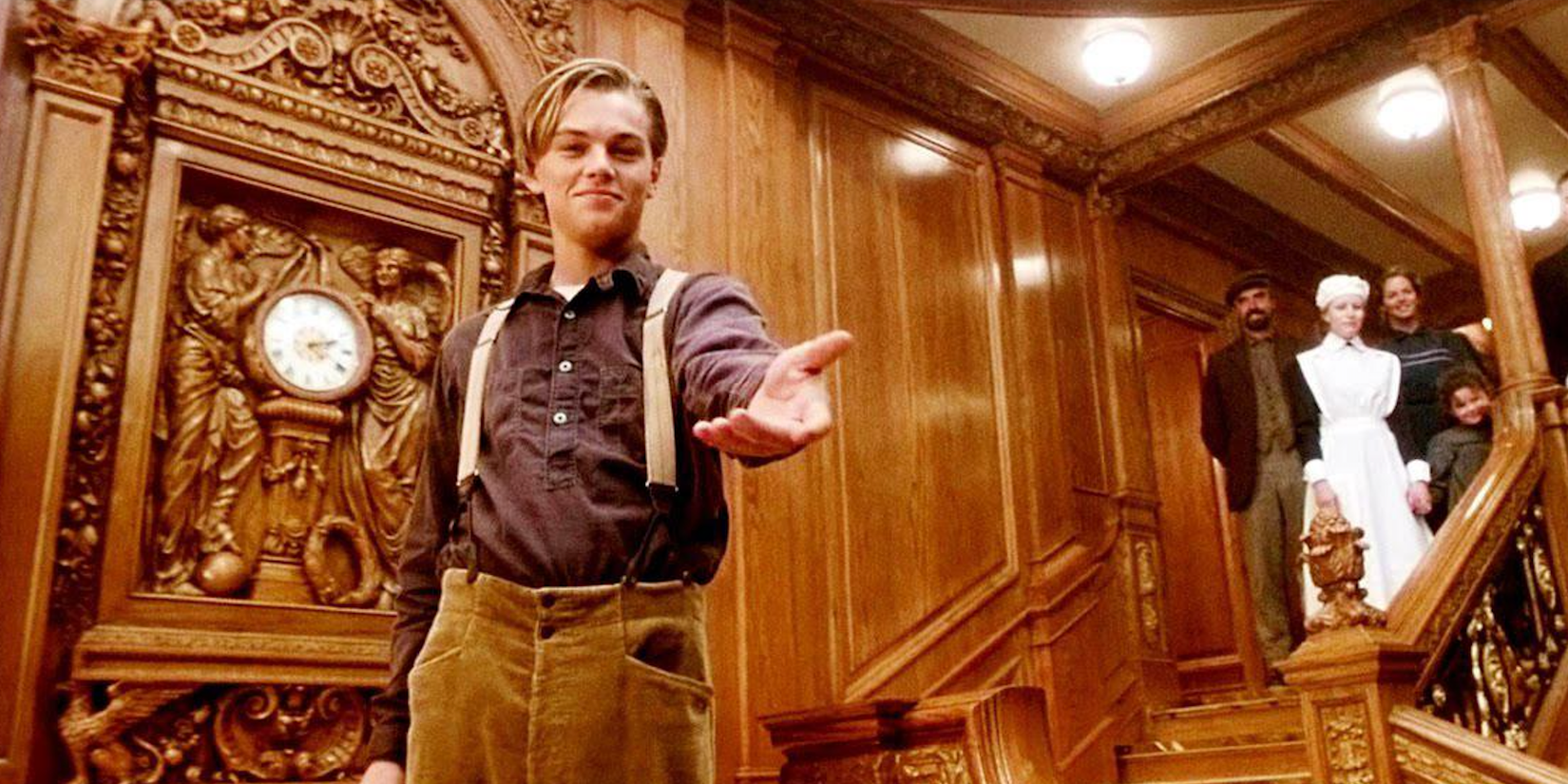 Leonardo DiCaprio stands on a grand staircase with a hand extended to camera in Titanic