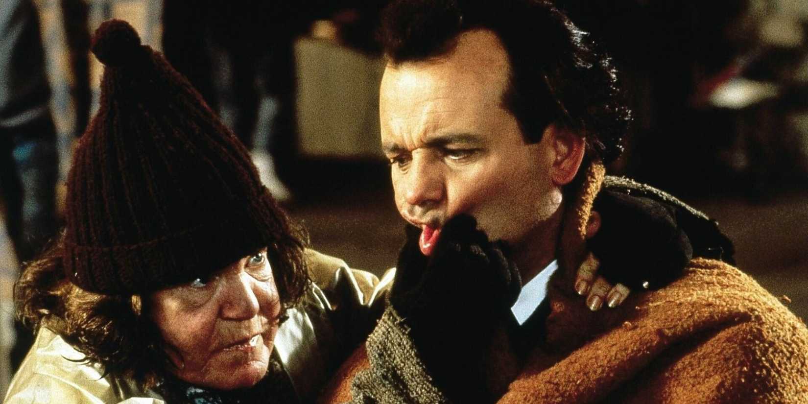 Bill Murray as Frank Cross has his cheeks squished by a costar in Scrooged.