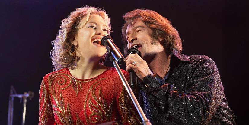 Claire and Mike Sardina singing together on stage in glittery red and black outfits.