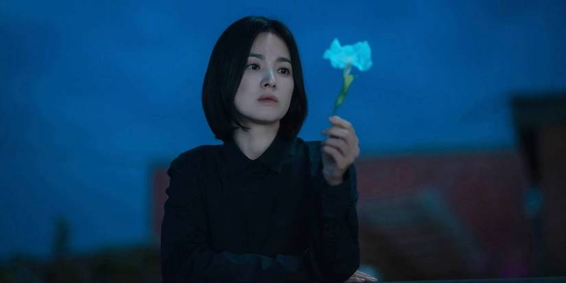 Song Hye-kyo holding and looking at a single flower in a scene from The Glory.
