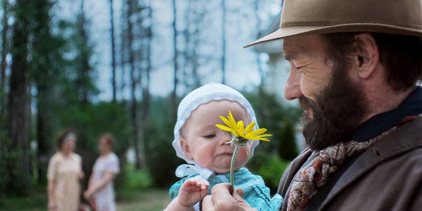 Robert is holding Kate, offering her a yellow flower, and smiling.