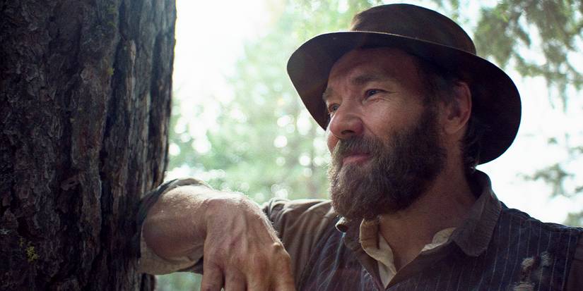 Robert is resting his elbow on a tree trunk, smiling.