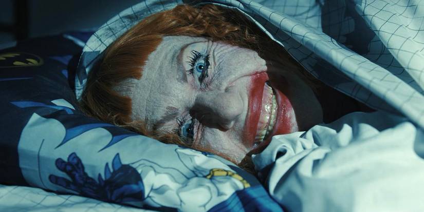 Amy Madigan smiling creepily under the bed covers in Weapons