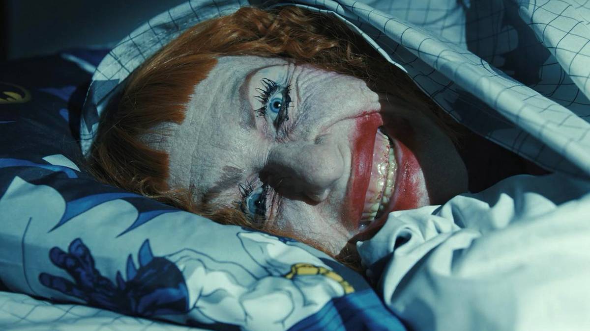 Amy Madigan smiling creepily under the bed covers in Weapons