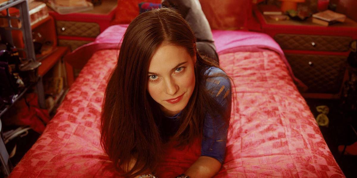 Jaye Tyler deitada em sua cama, olhando para a câmera com um sorriso em Wonderfalls.