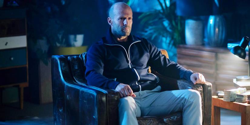 Jason Statham in Wrath of Man - he's sitting in a leather chair next to a small table filled with money