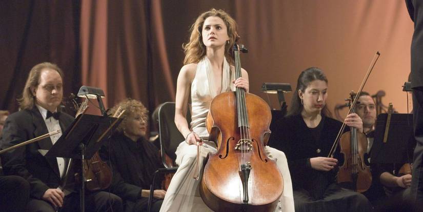 Lyla (Keri Russell) staring out from the stage as she holds a cello in her arms. 