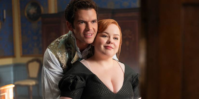 Luke Newton berdiri di belakang Nicola Coughlan saat mereka berpelukan dan tersenyum, melihat ke depan di Bridgerton Musim 4, Episode 1.