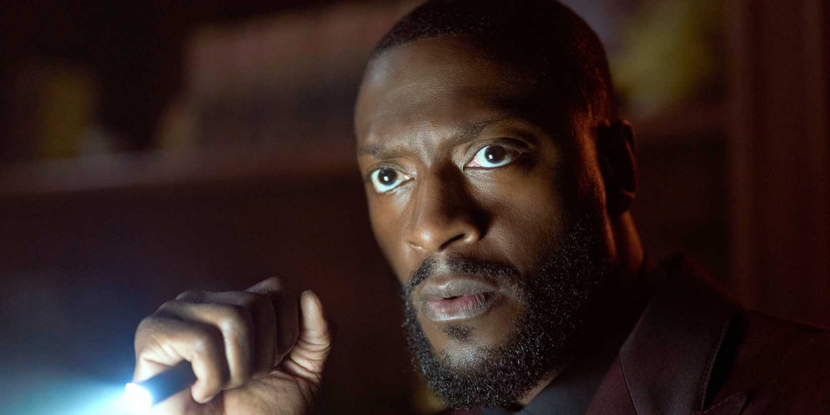 Aldis Hodge in Cross holding a flashlight.