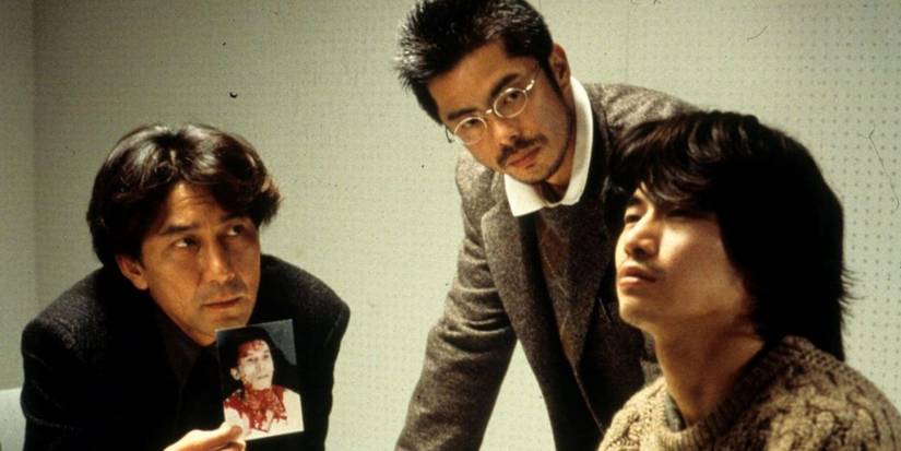 Two men showing a photo to a third in Cure-1997
