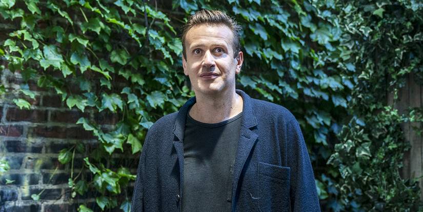 Jason Segel smiling in front of a brick wall in Dispatches From Eslewhere