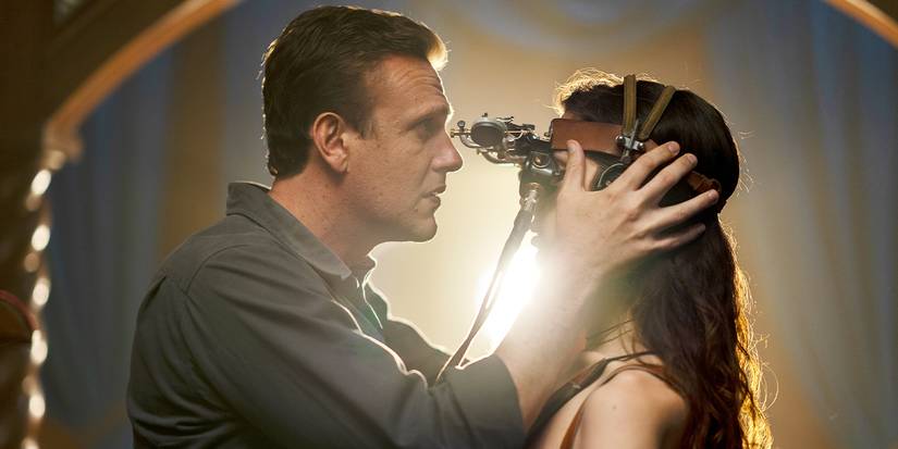 Jason Segel looking through a machine at Eve Lindley's head in Dispatches From Elsewhere